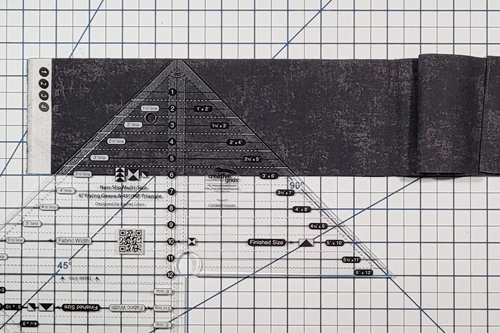 How to Make Flying Geese Step 8: Align quarter square triangle ruler measurement line that is the same width as the fabric strip along the bottom of the fabric strip.